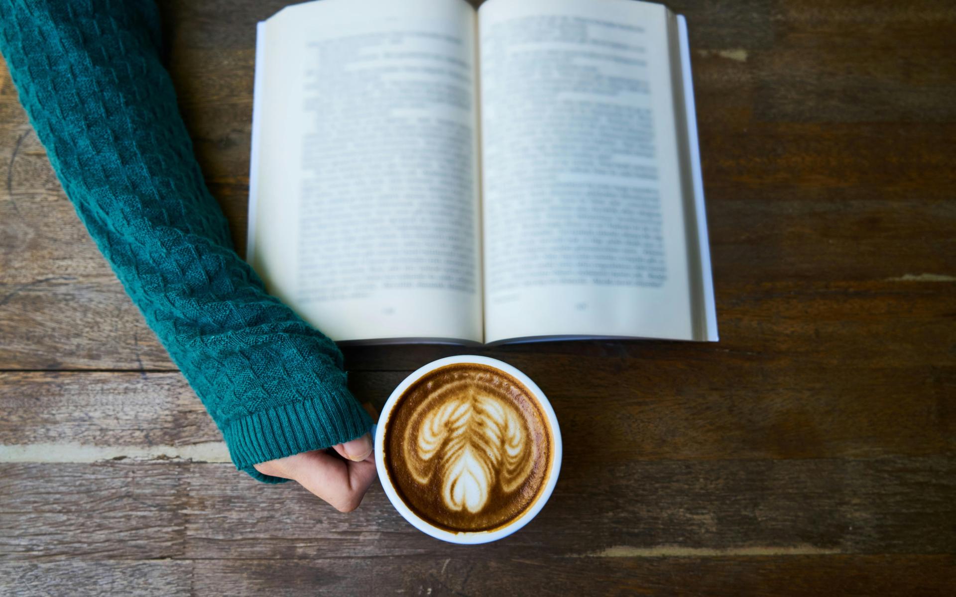 Hand hält eine Tasse Kaffee und man sieht auch ein Buch