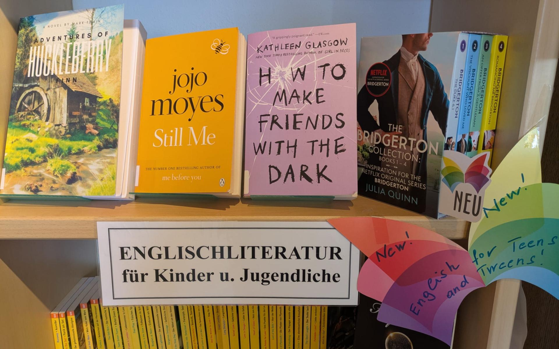 Regal mit neuen englischen Büchern für Kinder und Jugendliche, darunter „Huckleberry Finn“, „Still Me“ und die „Bridgerton“-Reihe, mit Schild „Englischliteratur für Kinder und Jugendliche“ und bunten „New!“-Hinweisen.